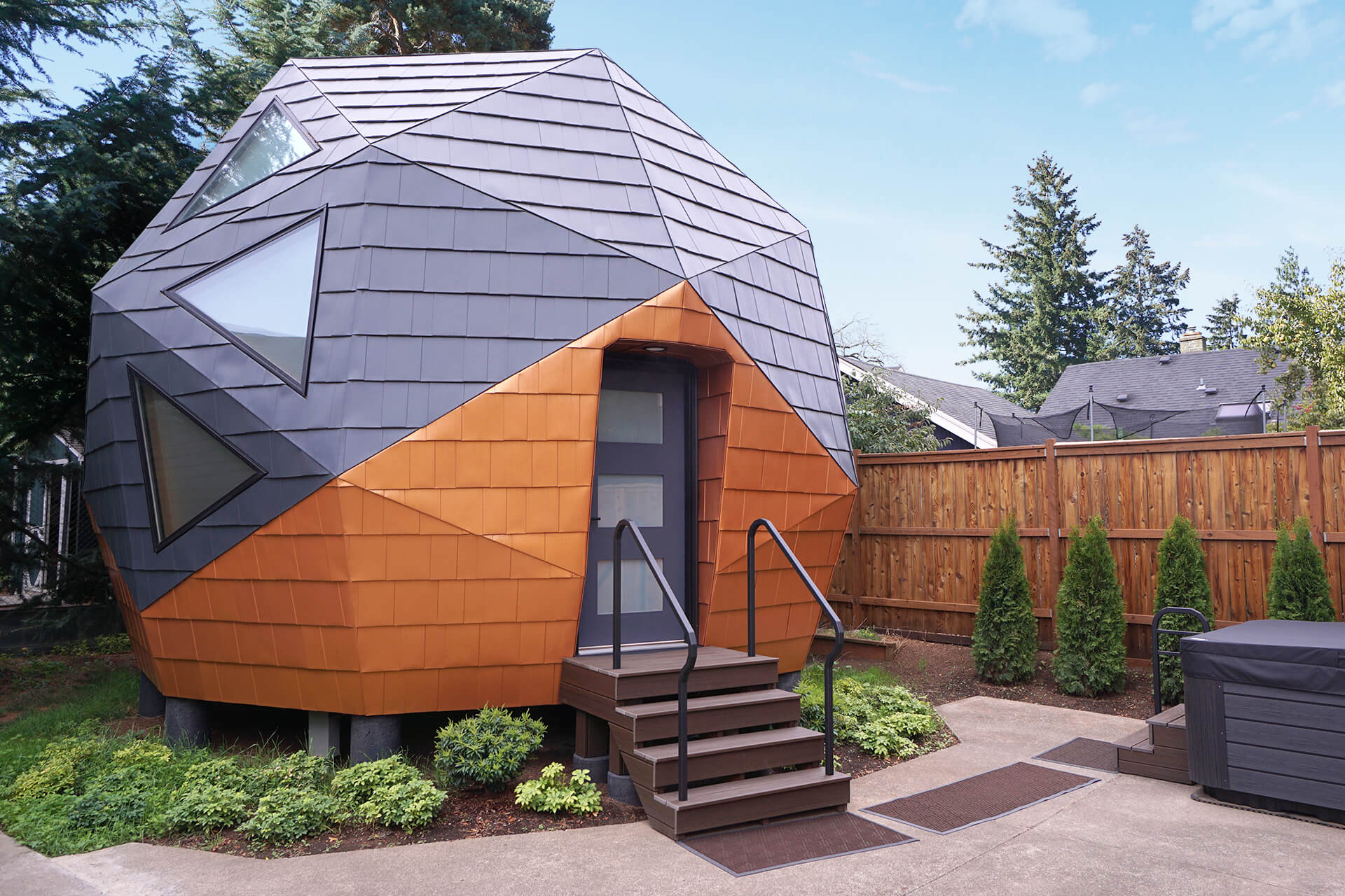 A mini geodesic dome home backyard adu, showcasing a modern and eco-friendly design with a four step front porch, surrounded by greenery and concrete.